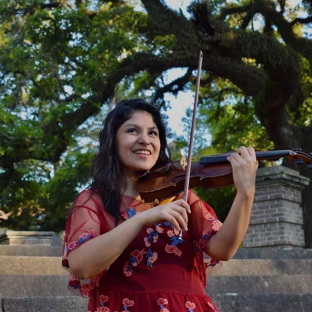 A Latin American woman wearing a red dress and playing the violin in a park.