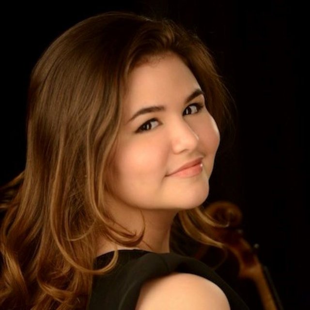 A headshot of a Mexican-American woman, looking over her shoulder to smile at the camera and holding a violin.