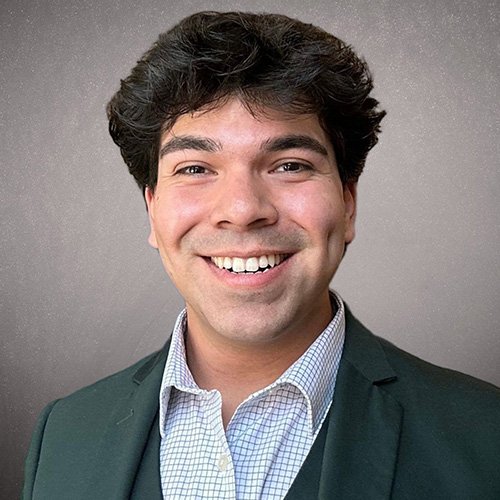 A headshot of a Mexican-American man, smiling broadly at the camera and wearing a green suit.