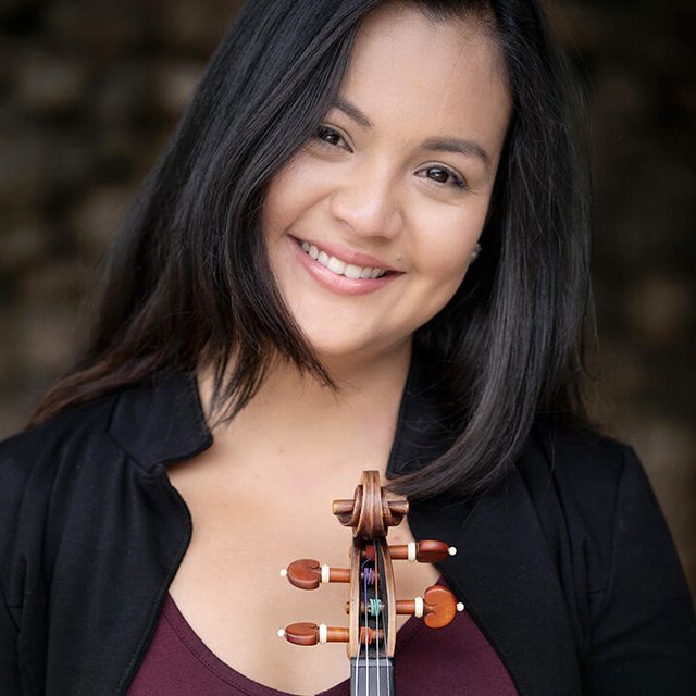 A woman with long dark hair and a warm smile holds a violin