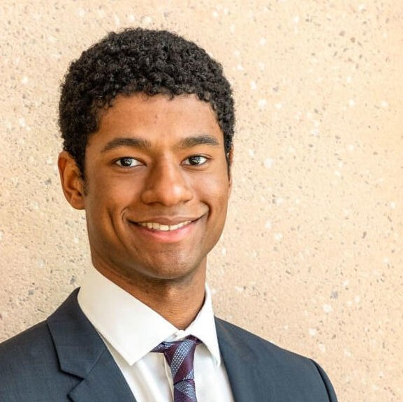 A young black man in a suit smiles at the camera