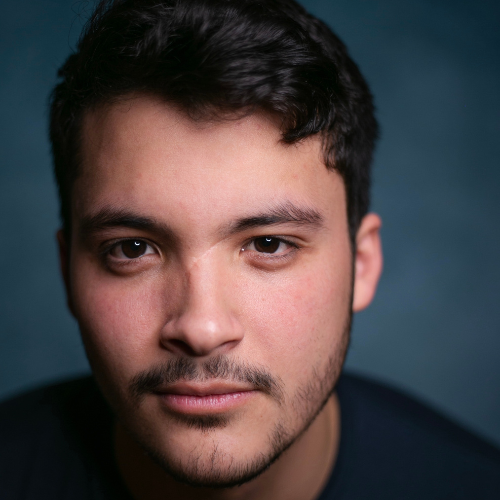 a young man with dark hair and facial hair looks directly into the camera