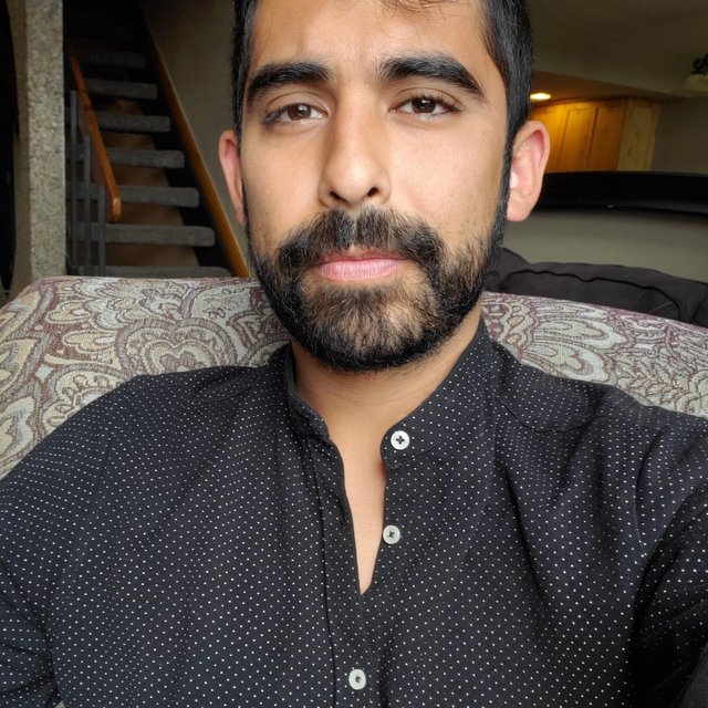 A man with dark facial hair wearing a dark shirt smiles at the camera
