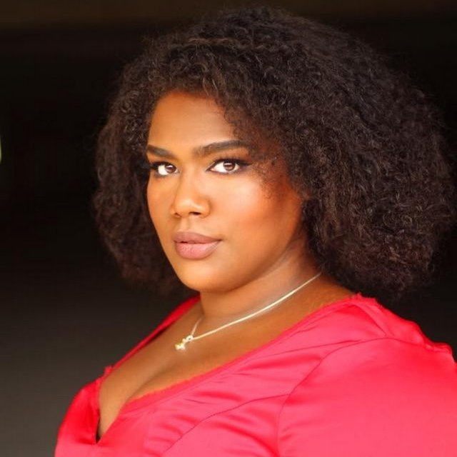 A portrait photo of a Black woman with a pink dress and a slight smile.