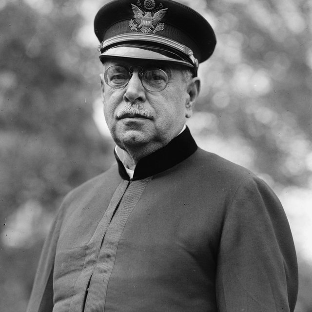 A black-and-white photo of a white man with a mustache and round glasses, wearing a military band uniform and a neutral expression.