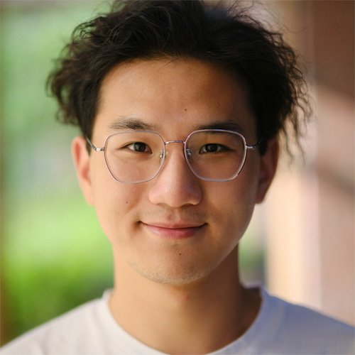 A headshot of a man of Chinese descent, wearing wire-frame glasses and smiling at the camera.