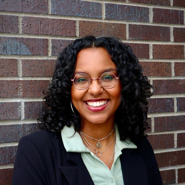 a young black woman with glasses and long hair smiles at the camera
