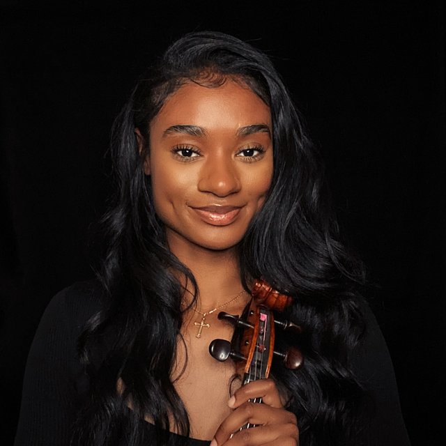A Black woman with long hair holding a viola and smiling.